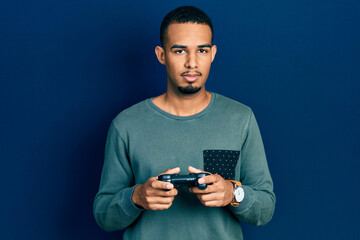 Young african american man playing video game holding controller relaxed with serious expression on face. simple and natural looking at the camera.