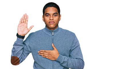 Young handsome hispanic man wearing casual sweatshirt swearing with hand on chest and open palm,...