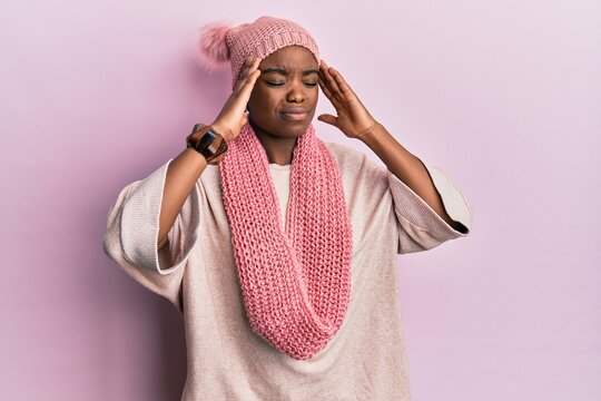Young african american woman wearing wool hat and winter scarf with hand on head, headache because stress. suffering migraine.