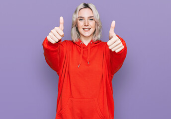 Young blonde girl wearing casual clothes approving doing positive gesture with hand, thumbs up smiling and happy for success. winner gesture.