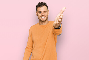 Young hispanic man wearing casual clothes smiling friendly offering handshake as greeting and welcoming. successful business.