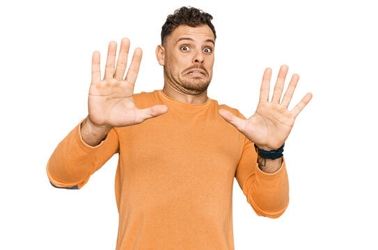 Young hispanic man wearing casual clothes afraid and terrified with fear expression stop gesture with hands, shouting in shock. panic concept.