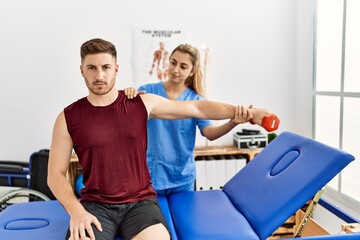 Obraz premium Young hispanic physioterapist woman make arm rehab treatment to man at the clinic.