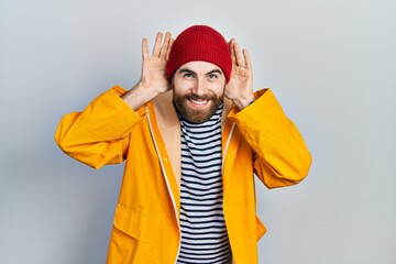 Caucasian man with beard wearing yellow raincoat smiling pulling ears with fingers, funny gesture. audition problem