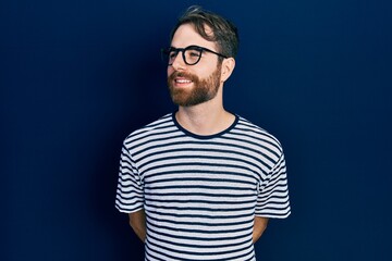 Obraz premium Caucasian man with beard wearing striped t shirt and glasses looking away to side with smile on face, natural expression. laughing confident.