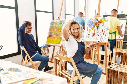 Group of middle age artist at art studio smiling confident touching hair with hand up gesture, posing attractive and fashionable