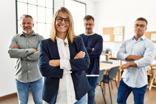 Middle age businesswoman smiling with arms crossed gesture standing with work partners at the office.