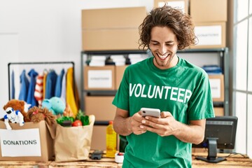 Young hispanic volunteer man smiling happy using smartphone at charity center.