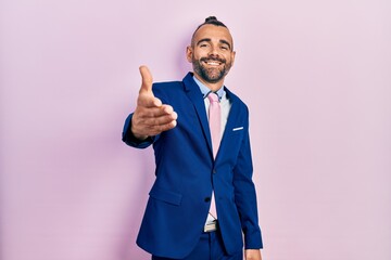Young hispanic man wearing business suit and tie smiling friendly offering handshake as greeting and welcoming. successful business.