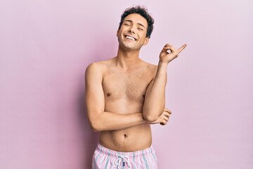 Fototapeta premium Young handsome man wearing swimwear shirtless with a big smile on face, pointing with hand and finger to the side looking at the camera.