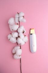 Ultrasonic Skin Scrubber Deep Face Cleaning Machine Peeling. Ultrasonic facial cleaner with a branch of cotton on pink background.