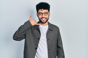 Young arab man with beard wearing glasses smiling doing phone gesture with hand and fingers like talking on the telephone. communicating concepts.