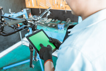 a bicycle mechanic wearing gloves uses a tablet digital while browsing in a workshop