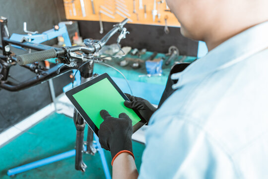 a bicycle mechanic wearing gloves uses a tablet digital while browsing in a workshop - Powered by Adobe
