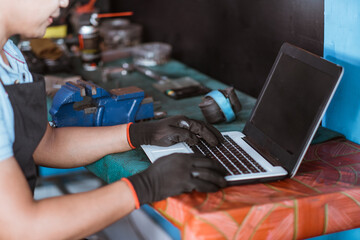 a bicycle mechanic wearing gloves uses a laptop computer while browsing in a workshop