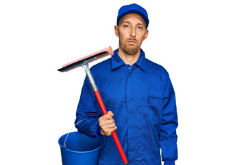 Bald man with beard wearing glass cleaner uniform and squeegee thinking attitude and sober...