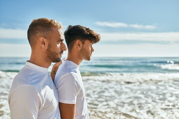 Young gay couple with serious expression looking to the horizon at the beach.