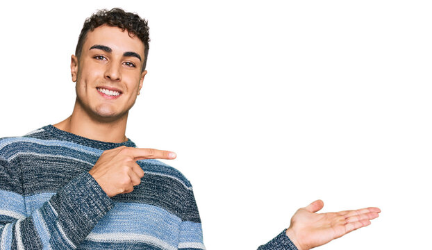 Hispanic young man wearing casual clothes amazed and smiling to the camera while presenting with hand and pointing with finger.