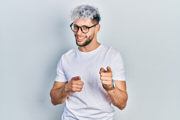 Young hispanic man with modern dyed hair wearing white t shirt and glasses pointing fingers to camera with happy and funny face. good energy and vibes.