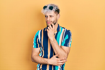 Young hispanic man with modern dyed hair wearing summer shirt and sunglasses thinking concentrated about doubt with finger on chin and looking up wondering