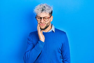 Young hispanic man with modern dyed hair wearing sweater and glasses touching mouth with hand with painful expression because of toothache or dental illness on teeth. dentist