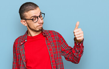 Hispanic young man wearing casual clothes looking proud, smiling doing thumbs up gesture to the side