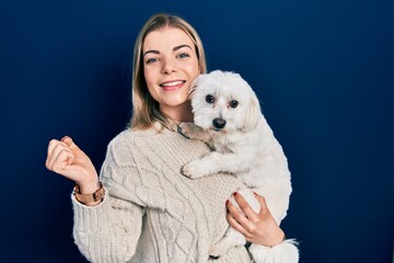 Beautiful caucasian woman hugging cute dog screaming proud, celebrating victory and success very excited with raised arm