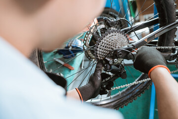 bicycle mechanic's hand with gloves uses an allen key to install the rear derailleur while working in a workshop - obrazy, fototapety, plakaty