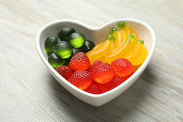 Delicious gummy fruit shaped candies on white wooden table