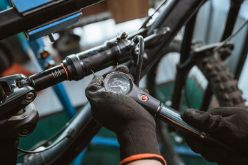 close up of a bicycle mechanic's hand in gloves using a pressure gauge pump to adjust the...