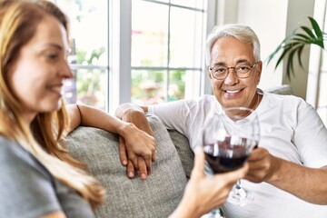 Middle age hispanic couple smiling happy drinking wine sitting on the sofa at home.