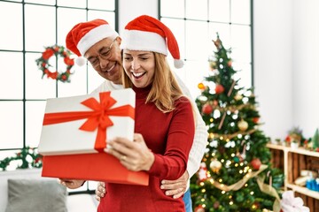 Obraz na płótnie Canvas Middle age hispanic couple smiling happy and hugging unboxing christmas gift at home.