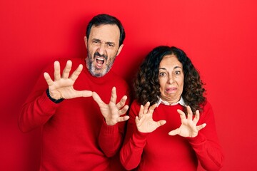 Middle age couple of hispanic woman and man hugging and standing together afraid and terrified with fear expression stop gesture with hands, shouting in shock. panic concept.