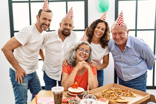 Group of middle age friends celebrate birthday looking at the camera at home.