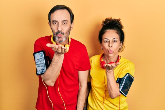 Middle age couple of hispanic woman and man wearing sportswear and arm band looking at the camera blowing a kiss with hand on air being lovely and sexy. love expression.