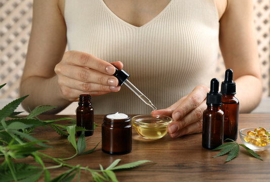 Woman dripping THC tincture or CBD oil into bowl at wooden table, closeup