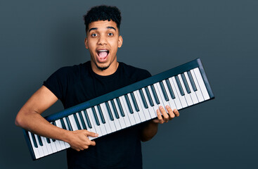 Young african american man holding piano keyboard celebrating crazy and amazed for success with...