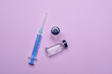 Disposable syringe and vials with medicine on violet background, flat lay