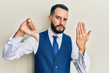 Young man with beard wearing engagement ring with angry face, negative sign showing dislike with thumbs down, rejection concept