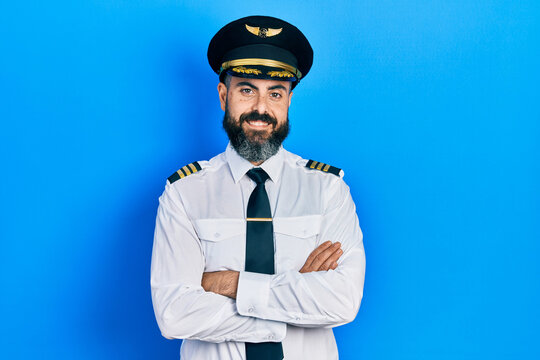 Young hispanic man wearing airplane pilot uniform with arms crossed gesture smiling with a happy and cool smile on face. showing teeth.