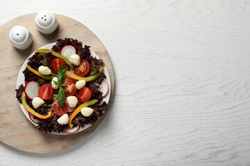 Delicious vegetable salad with mozzarella served on white wooden table, top view. Space for text