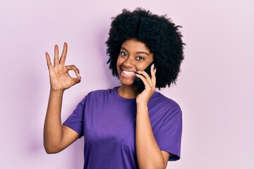 Fototapeta na wymiar Young african american woman having conversation talking on the smartphone doing ok sign with fingers, smiling friendly gesturing excellent symbol