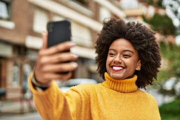 Fototapeta na wymiar Young african american girl smiling happy making selfie by the smartphone at the city.