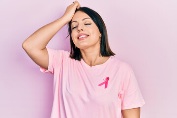 Young hispanic woman wearing pink cancer ribbon on t shirt smiling confident touching hair with hand up gesture, posing attractive and fashionable