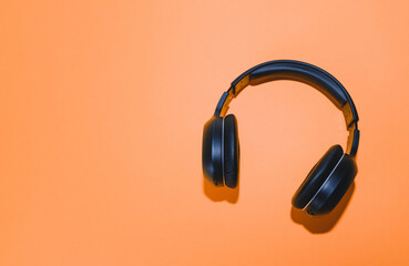 Black wireless headphones isolated on an orange background. 