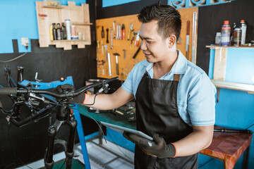 Portrait of a repairman in an apron as work clothes using a tablet to repair in a bicycle repair shop