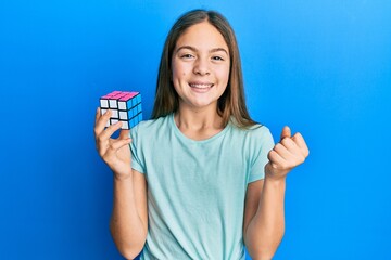 Beautiful brunette little girl playing colorful puzzle cube intelligence game screaming proud,...