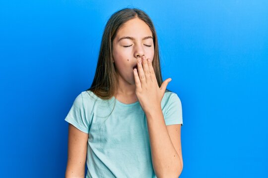 Beautiful brunette little girl wearing casual white t shirt bored yawning tired covering mouth with hand. restless and sleepiness.
