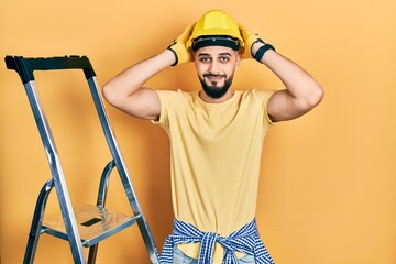 Handsome man with beard by construction stairs wearing hardhat doing bunny ears gesture with hands palms looking cynical and skeptical. easter rabbit concept.