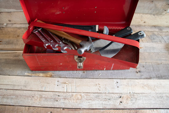 Old red retro handyman toolbox on wooden background.